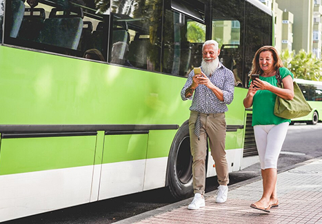 two passengers waiting in the street for a green charter bus to depart