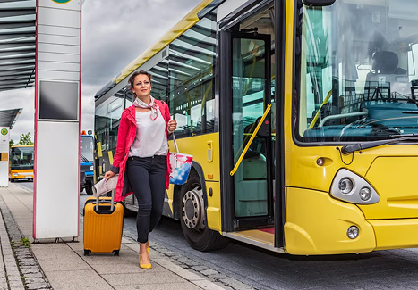 a passenger waiting in the street with her luggage for a yellow charter bus to depart