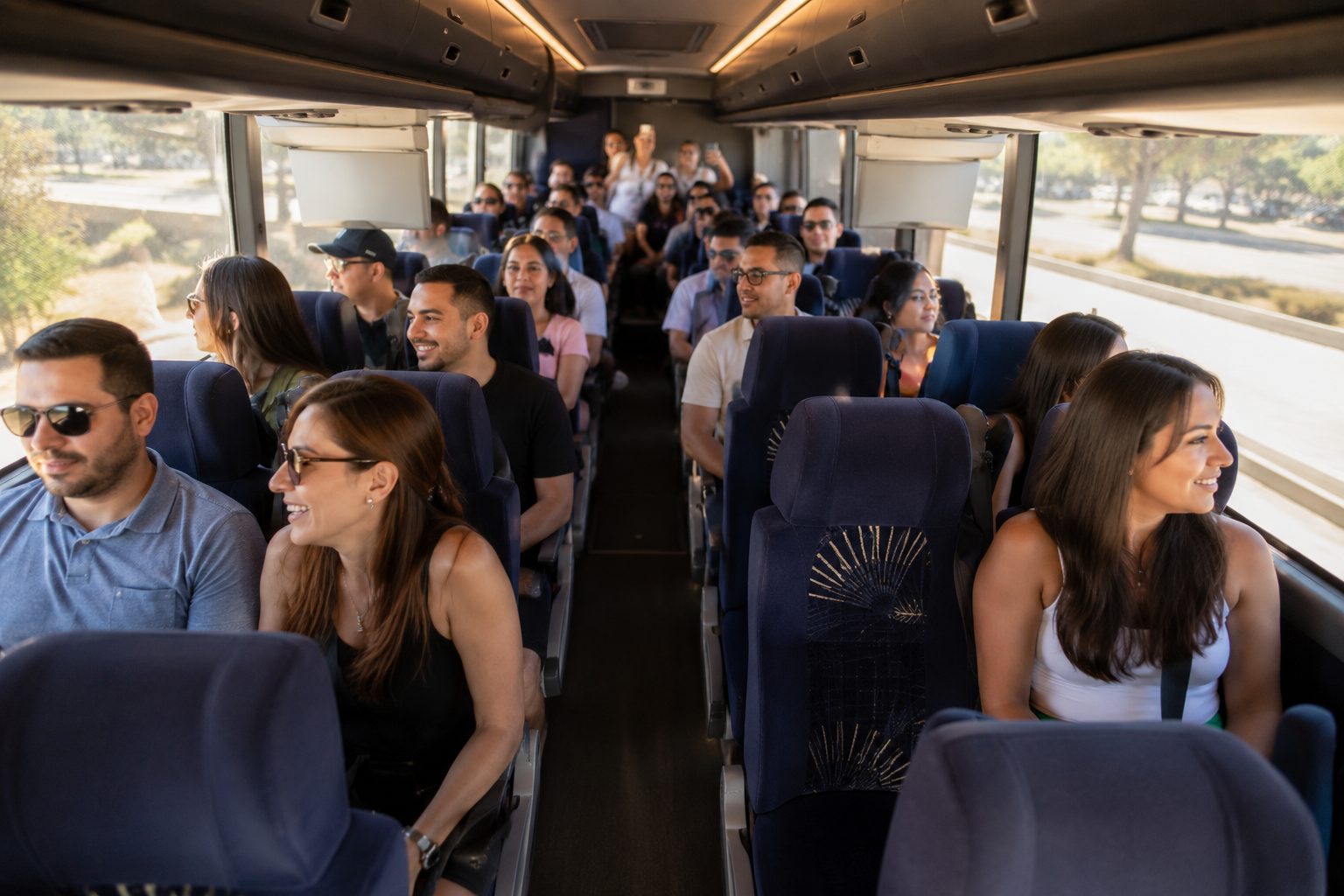 Diverse group of happy passengers seated inside a full-size charter bus traveling to a Los Angeles sporting event