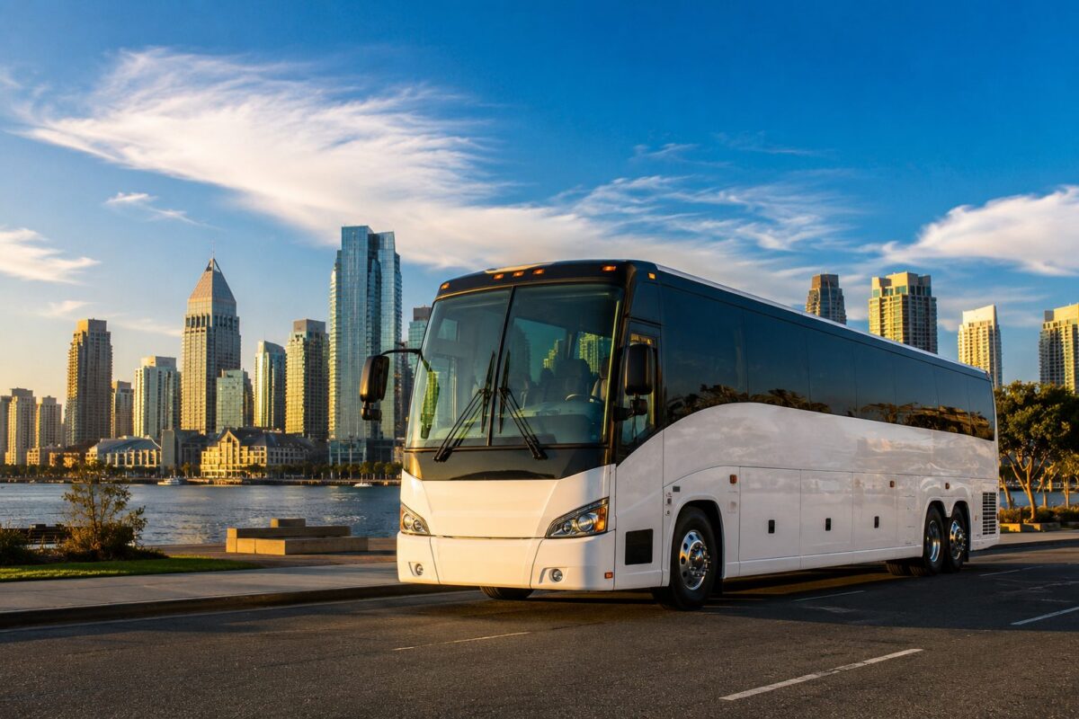 White full-size charter bus parked at Coronado waterfront with San Diego downtown skyline at golden hour, ready for FIFA World Cup 2026 group transport to SoFi Stadium Los Angeles