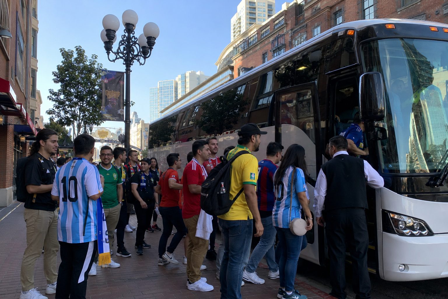 Diverse group of soccer fans in national team jerseys boarding a charter bus in San Diego Gaslamp Quarter for FIFA World Cup 2026 trip to SoFi Stadium Los Angeles