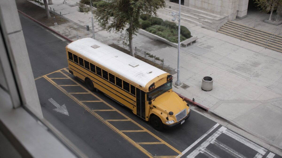 Yellow school field trip bus parked in a designated loading zone outside a Los Angeles building, aerial view