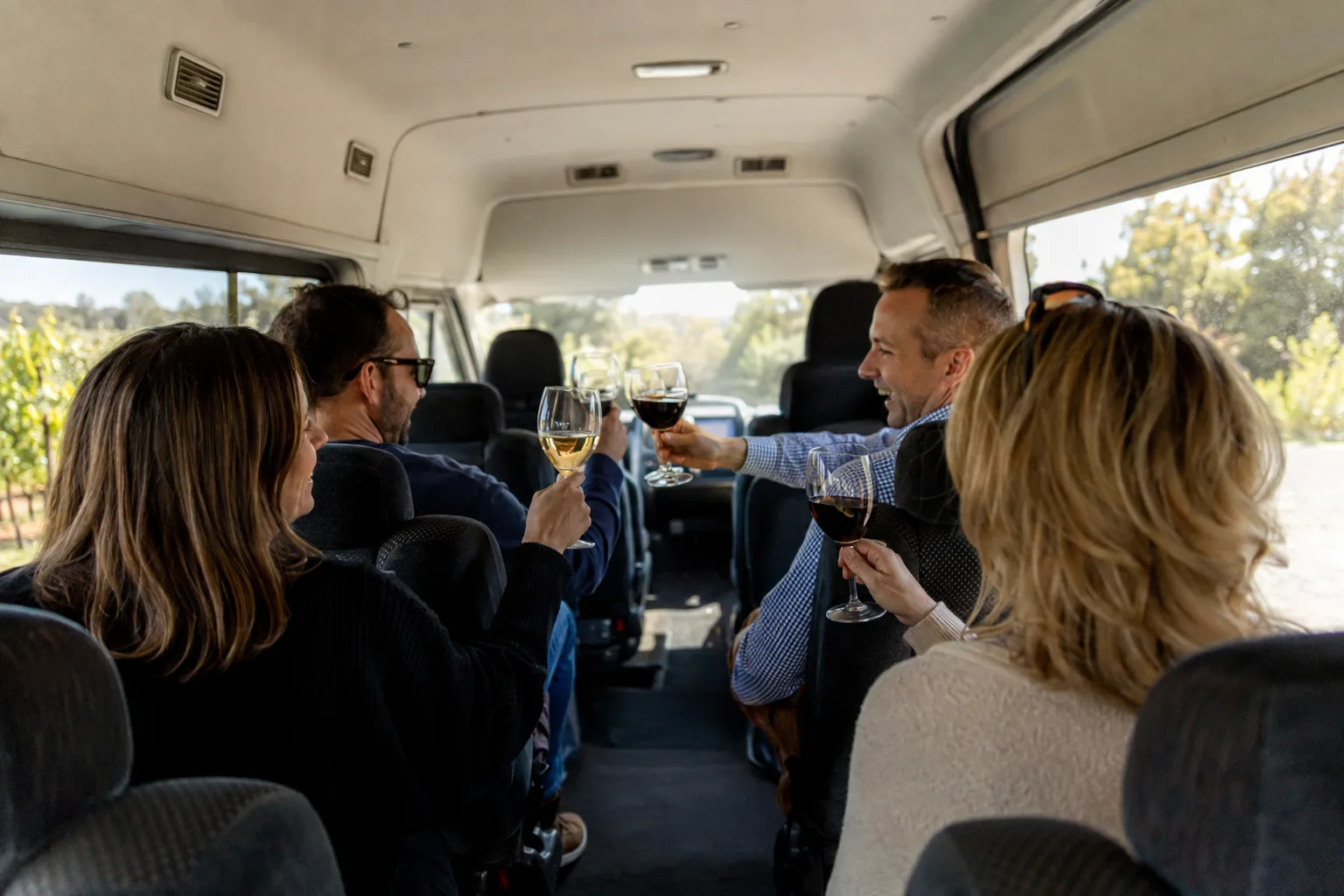 Small group toasting wine glasses together inside a shuttle van during a Temecula wine tour